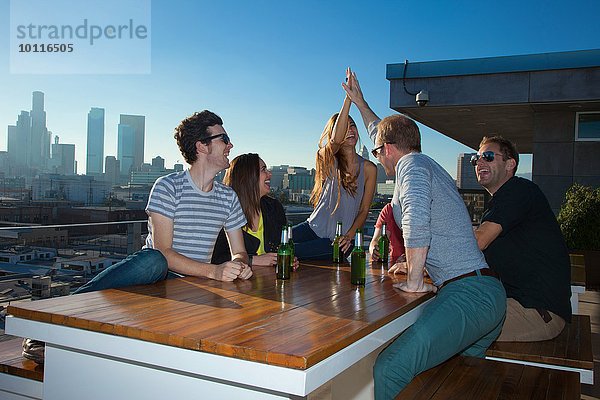 Sechs erwachsene Freunde trinken Bier am Tisch der Dachbar mit Skyline von Los Angeles  USA