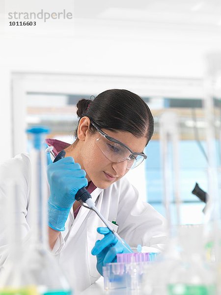 Junge Wissenschaftlerin pipettiert Probe in ein Fläschchen in einem Labor für chemische und DNA-Tests.