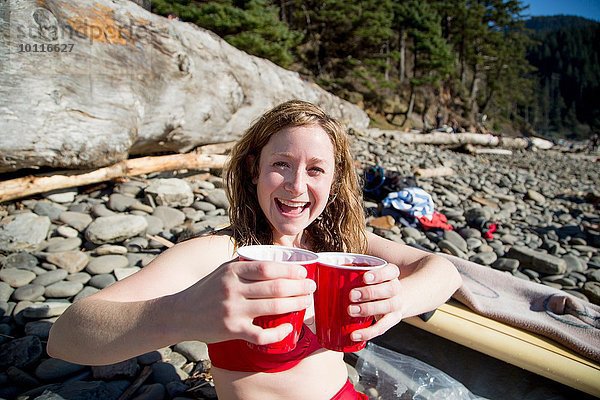 Junge Frau am Felsenstrand sitzend  Getränke haltend  lächelnd  Short Sands Beach  Oregon  USA