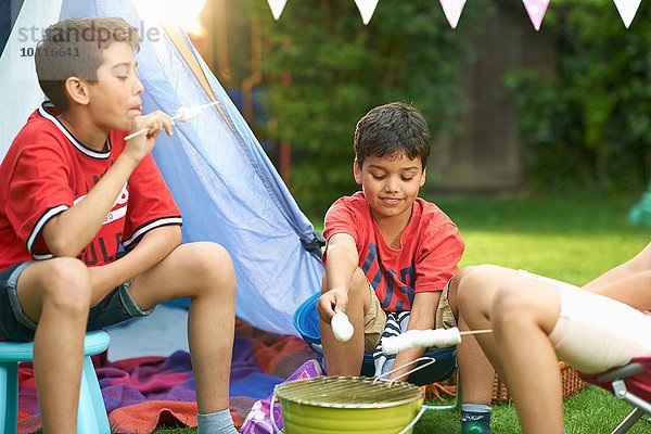 Mädchen und Brüder rösten Marshmallows vor hausgemachtem Zelt im Garten