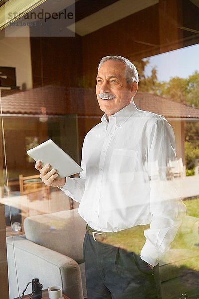 Älterer Mann zu Hause  der ein digitales Tablet hält