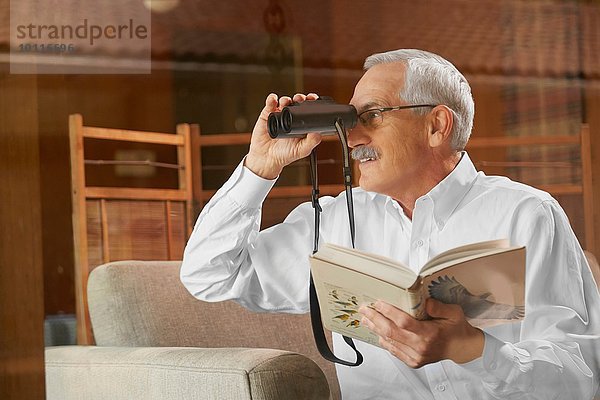 Älterer Mann zu Hause  Vogelbeobachtung durch Fenster  Benutzung eines Fernglases