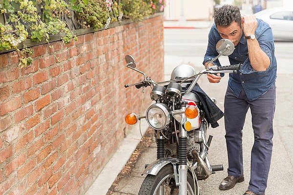 Mittlerer Erwachsener Mann  der die Haare im Seitenspiegel des Motorrads überprüft.