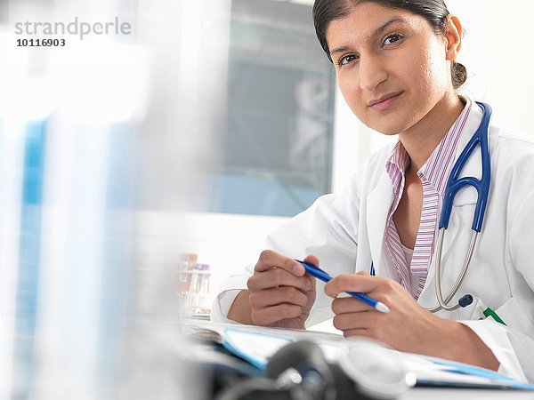 Porträt einer Ärztin am Schreibtisch bei der Arbeit an Krankenakten