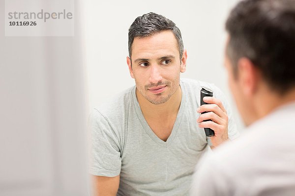 Mittlerer erwachsener Mann  der in den Spiegel schaut und einen elektrischen Rasierer benutzt.