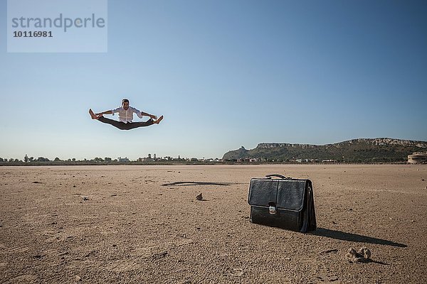 Mittlerer Erwachsener Geschäftsmann  der am Strand in die Luft springt.