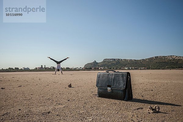 Mittlerer erwachsener Geschäftsmann beim Radfahren am Strand