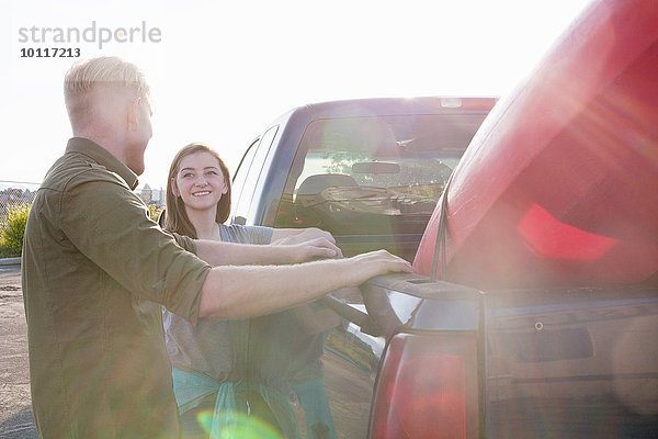 Junges Paar  das sich gegen den Pick-Up lehnt und sich lächelnd ansieht.