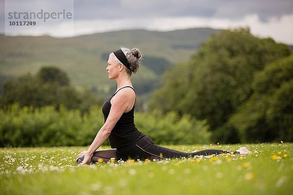 Reife Frau macht Spagat und übt Yoga-Position im Feld.
