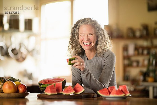 Porträt einer reifen Frau beim Essen von Wassermelone in der Küche