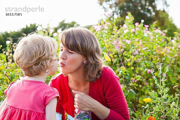 Mittlere erwachsene Mutter und Kleinkind Tochter beim Küssen im Blumenfeld