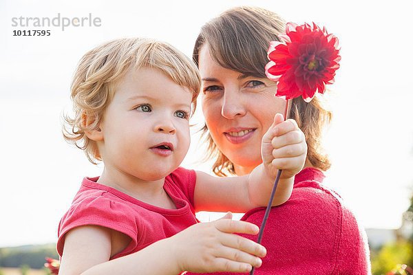 Porträt der mittleren erwachsenen Mutter und Kleinkindstochter mit roter Blume im Feld