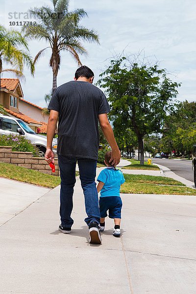 Rückansicht des jungen Mannes und des Kleinkindbruders beim Spaziergang über den Bürgersteig am Stadtrand