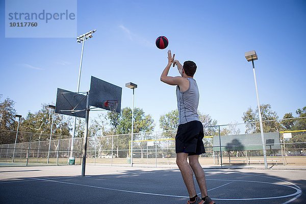 Junger Basketballspieler  der den Ball in Richtung Basketballkorb wirft.