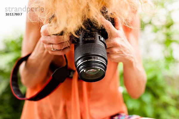 Abgeschnittene Aufnahme einer Frau mit roten Haaren  die mit der digitalen Spiegelreflexkamera nach unten fotografiert.