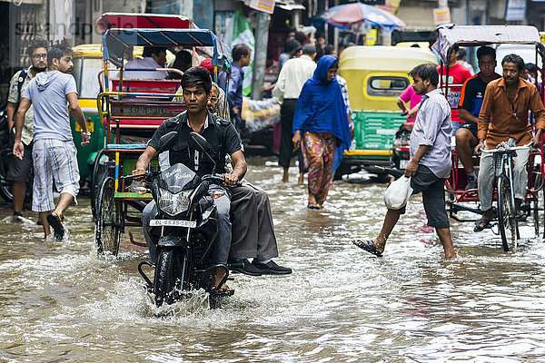 Menschen gehen und Motorräder und Fahrrad-Rikschas fahren durch die nach einem heftigen Monsunregenfall überfluteten Straßen der Vorstadt Paharganj  Neu-Delhi  Delhi  Indien  Asien