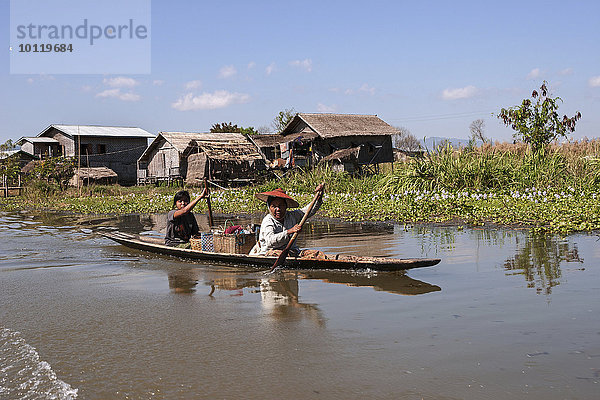 Traditionelle Stelzenhäuser im Inle-See  vorne zwei einheimische Frauen in einem Holzboot  Shan-Staat  Myanmar  Asien