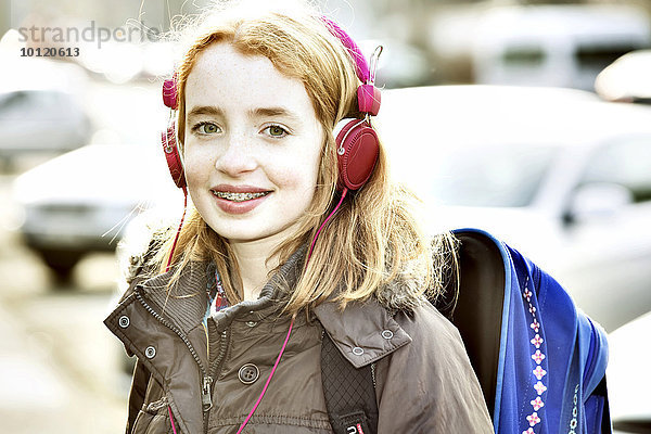 Mädchen mit Schulranzen und Kopfhörern auf dem Schulweg