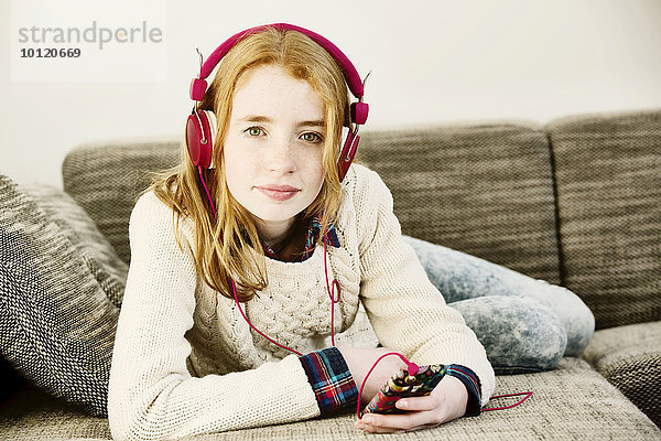 Mädchen liegt auf dem Sofa und hört Musik mit Kopfhörern mit ihrem Smartphone