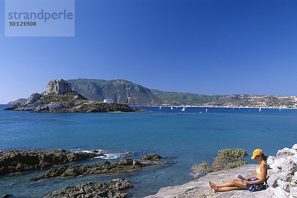 Touristin sitzt an der Küste mit Blick auf Agios Stefanos  Insel Kos  Dodekanes  Griechenland  Europa