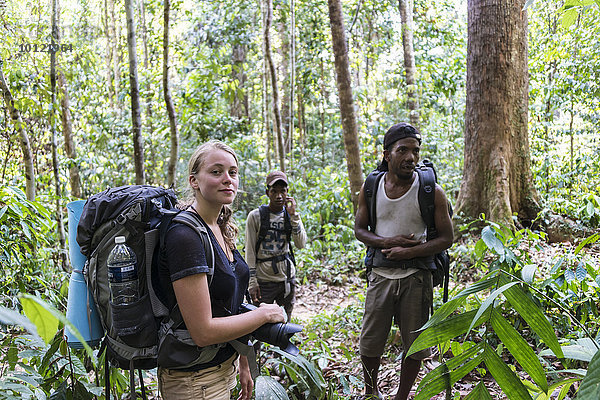 Touristin  Wanderin  Junge Frau mit Rucksack steht mit zwei Männern der Orang Asil im Dschungel  Nationalpark Taman Negara  Malaysia  Asien
