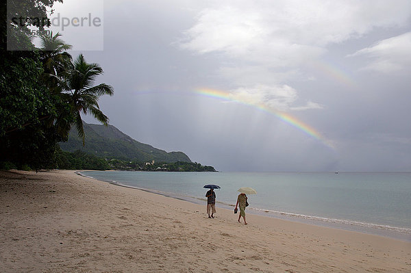 Zwei Menschen zu Fuß unter einem Regenbogen  am Indischen Ozean  Mahé  Seychellen  Afrika
