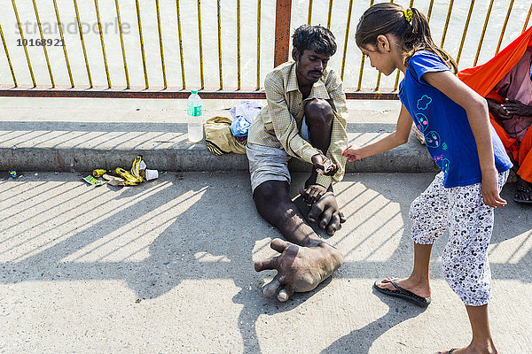 Ein Bettler mit Elephantiasis in seinen Füßen erhält Geld von einem Mädchen  Harki Pauri Ghat am Ganges  Haridwar  Uttarakhand  Indien  Asien