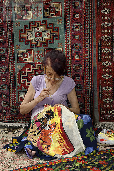 Frau stickt vor einem armenischen Teppich an einem Bildteppich  Markt  Jerewan  Armenien  Asien