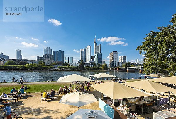 Leute in einem Gartenlokal am Ufer des Mains  hinten das Bankenviertel  Skyline von Frankfurt am Main  Hessen  Deutschland  Europa