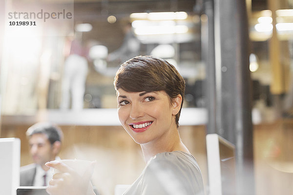Lächelnde Geschäftsfrau beim Kaffeetrinken im Büro