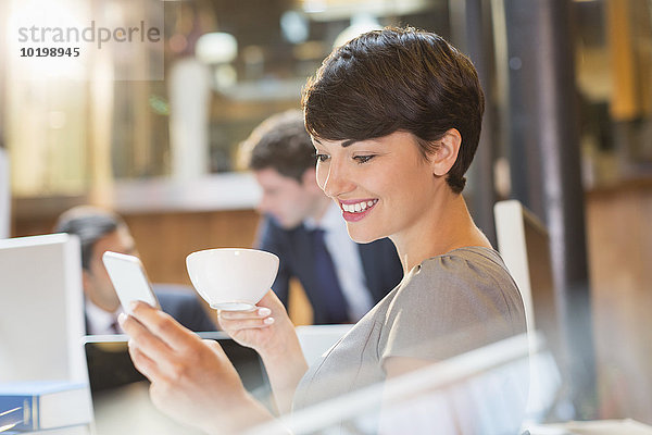 Geschäftsfrau trinkt Kaffee und SMS mit Handy im Büro