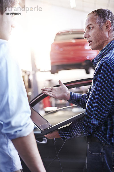 Mechaniker mit Laptop im Gespräch mit dem Kunden in der Kfz-Werkstatt