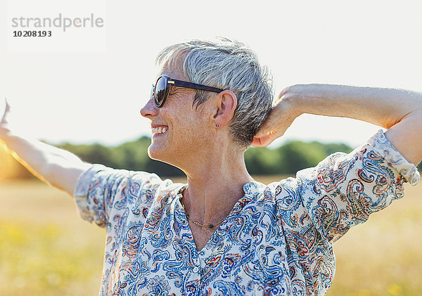 Enthusiastische Seniorin mit ausgestreckten Armen im sonnigen Feld