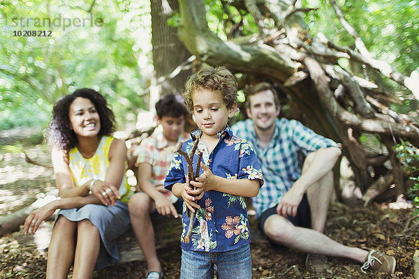 Familie beobachtet Jungen spielen mit Stöcken im Wald