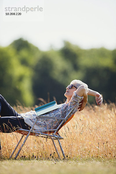 Sorglose Seniorin entspannt mit Buch im sonnigen Feld