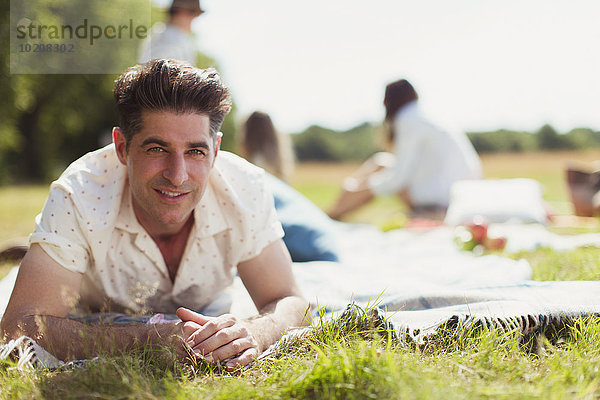 Portrait lächelnder Mann auf Picknickdecke im sonnigen Feld liegend