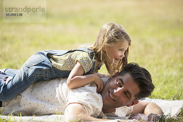 Verspielte Tochter auf dem Vater im sonnigen Feld liegend