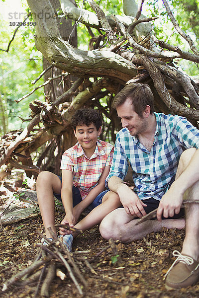 Vater und Sohn machen ein kleines Lagerfeuer mit Stöcken im Wald.