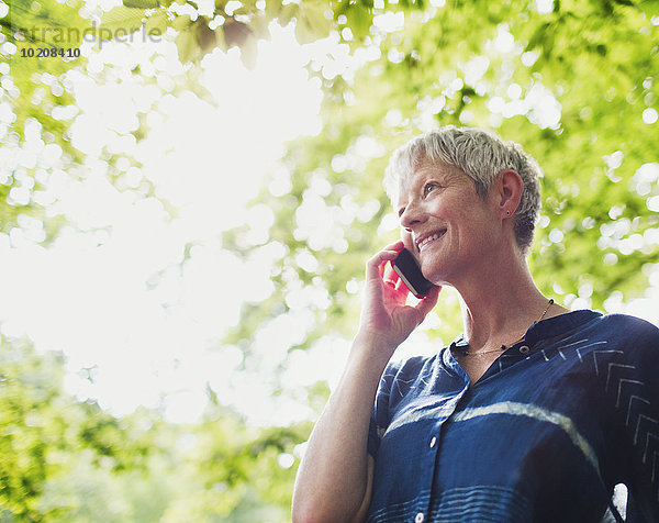 Lächelnde Seniorin beim Telefonieren unter Bäumen