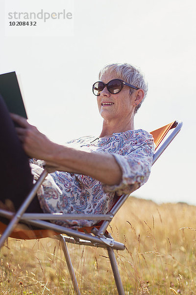 Seniorin liest Buch im sonnigen Feld