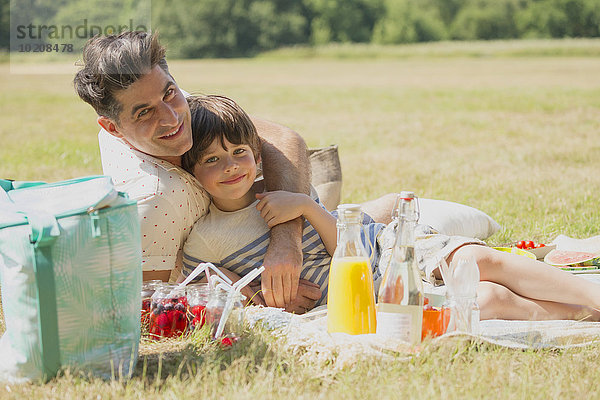 Portrait liebevoller Vater und Sohn entspannt auf Picknickdecke im sonnigen Feld