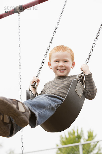 sitzend schaukeln schaukelnd schaukelt schwingen schwingt schwingend Europäer Junge - Person Spielplatz Schaukel