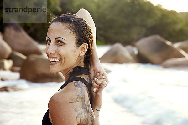Seychellen  Porträt einer lächelnden Frau mit Tatoo beim Yoga am Strand