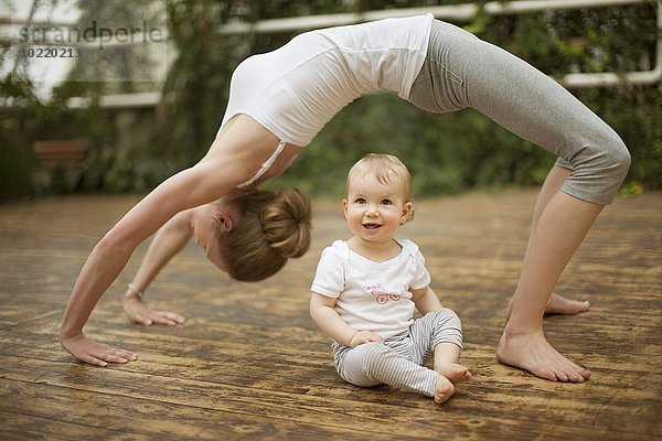 Frau macht Yoga-Übungen  während das Baby sie beobachtet.
