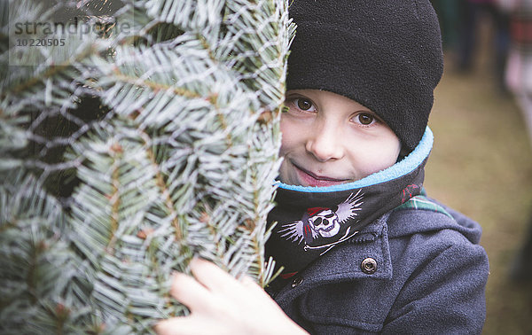 Portrait des Jungen mit eingewickeltem Weihnachtsbaum