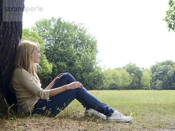 Junge Frau auf einer Wiese sitzend auf einem Baumstamm lehnend