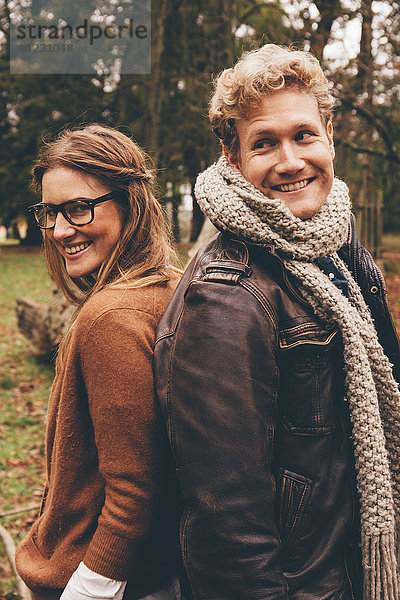 Ein glückliches junges Paar steht Rücken an Rücken in einem herbstlichen Park.