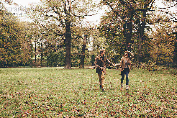 Junges verliebtes Paar hält sich an den Händen und läuft in einem herbstlichen Park.