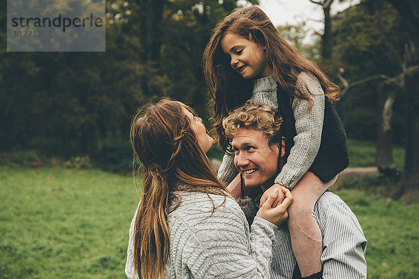 Glückliches junges Paar mit kleinem Mädchen auf den Schultern ihres Vaters im Herbstpark