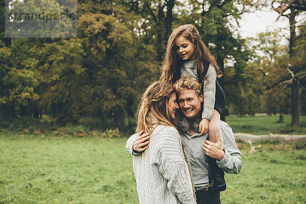 Junges Paar mit kleinem Mädchen auf den Schultern ihres Vaters im Herbstpark